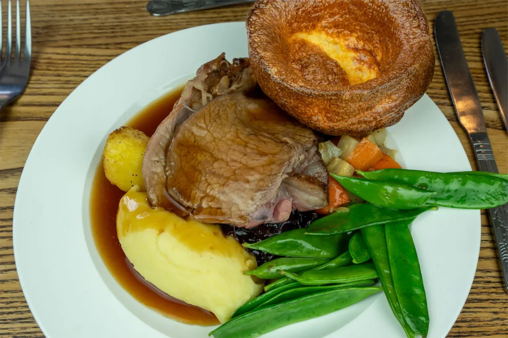A hearty Sunday roast at The Plough Inn Hathersage featuring perfectly roasted meats, golden crispy potatoes, Yorkshire puddings, seasonal vegetables, and rich homemade gravy — the perfect Peak District pub lunch.