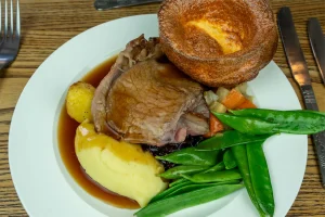 A hearty Sunday roast at The Plough Inn Hathersage featuring perfectly roasted meats, golden crispy potatoes, Yorkshire puddings, seasonal vegetables, and rich homemade gravy — the perfect Peak District pub lunch.