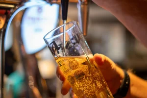 Bartender pouring a freshly pulled pint of lager at The Plough Inn, Hathersage in the Peak District