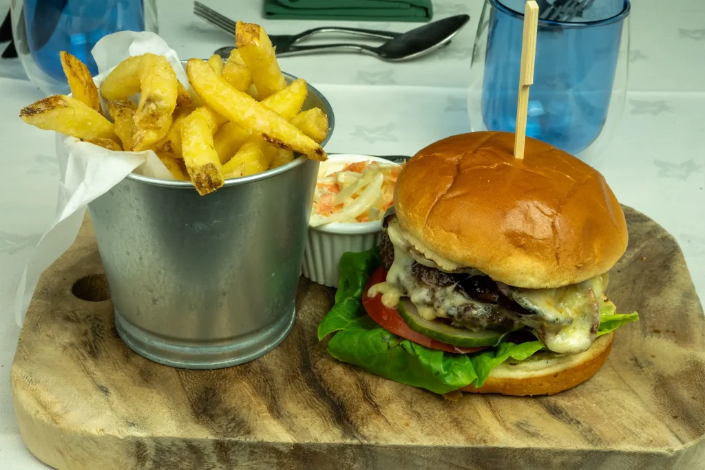 Handcrafted beef burger with melted cheese, salad, golden fries, and homemade slaw served at The Plough Inn, Hathersage in the Peak District