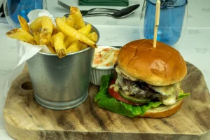 Handcrafted beef burger with melted cheese, salad, golden fries, and homemade slaw served at The Plough Inn, Hathersage in the Peak District